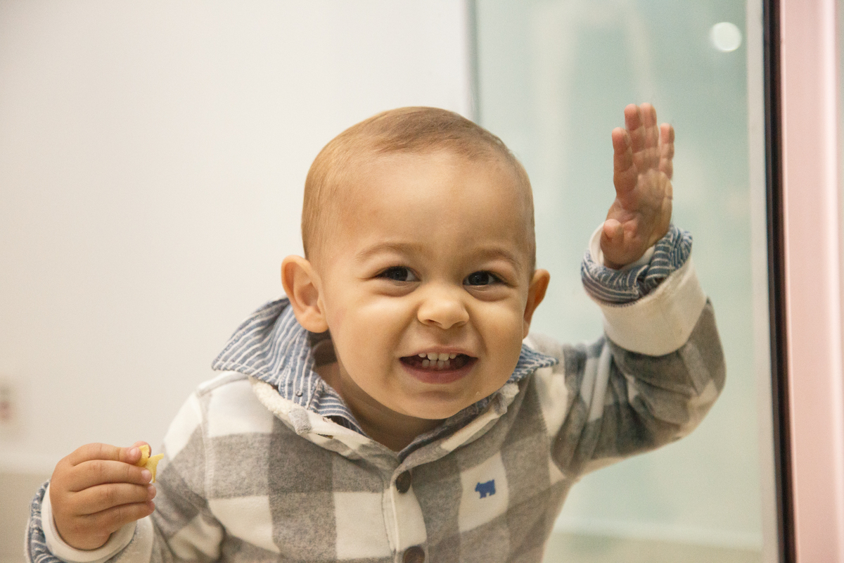 Criança brincando através de um vidro, fazendo careta, sorrindo para a foto.