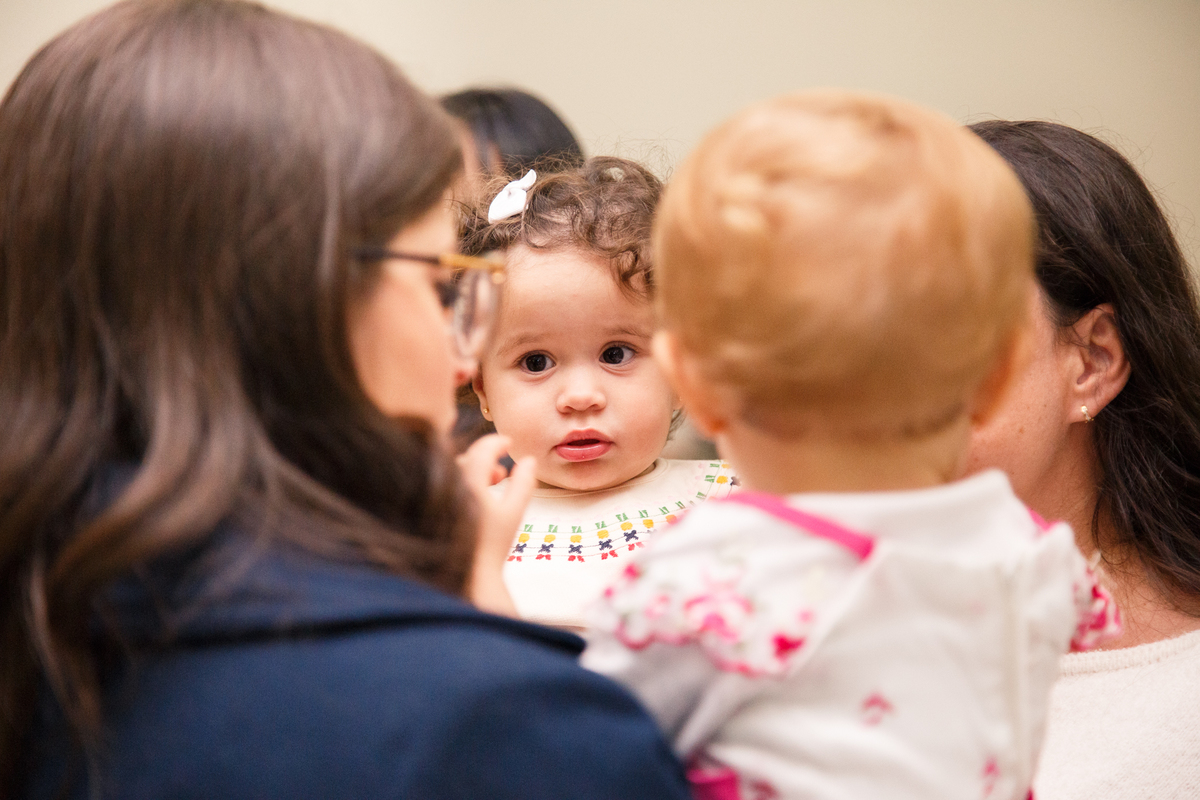 Foco no rosto de uma criança que pode ser visto entre duas cabeças que estão fora de foco no primeiro plano.