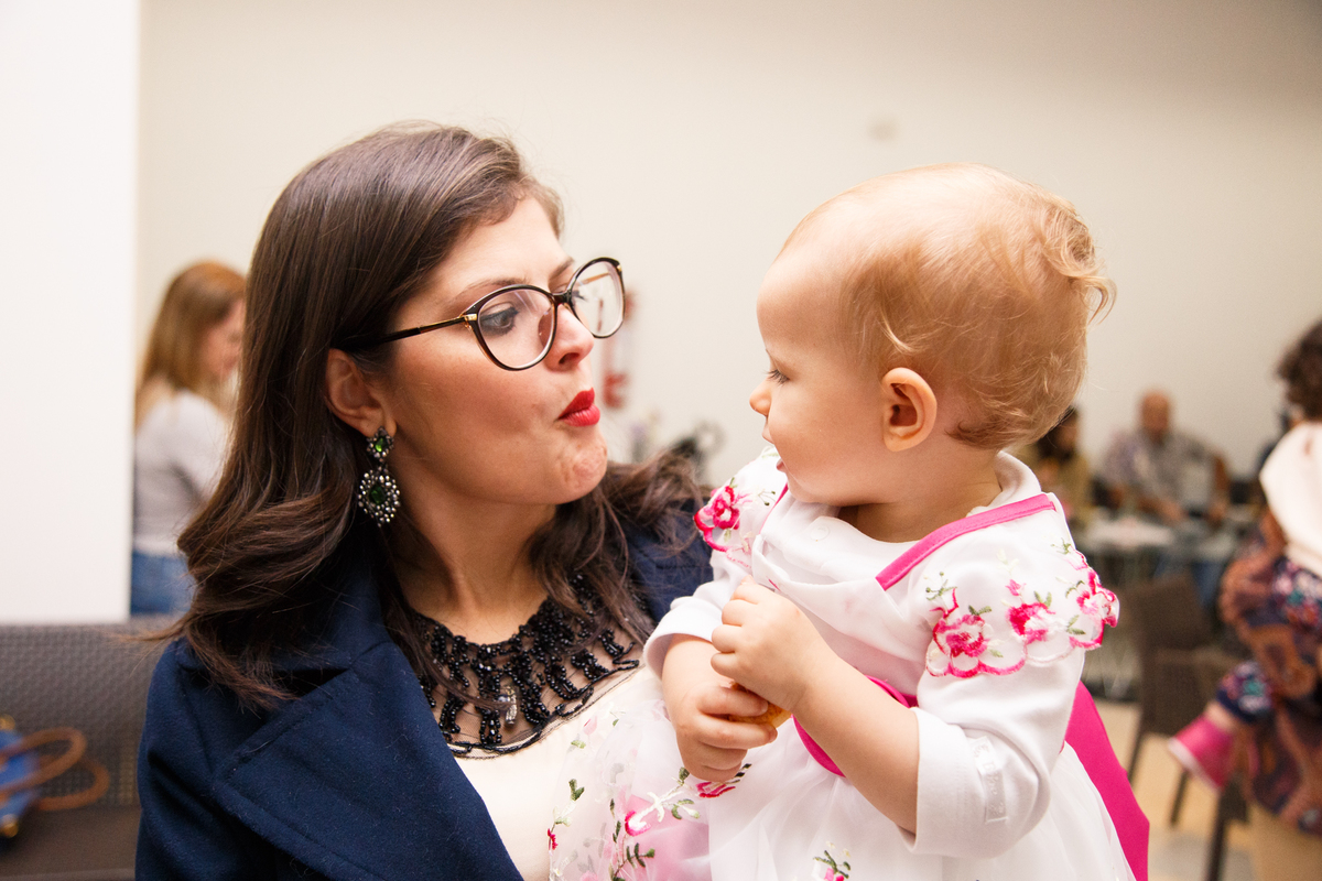 Tia e a bebê aniversariante no colo, fazendo caretas e brincando.