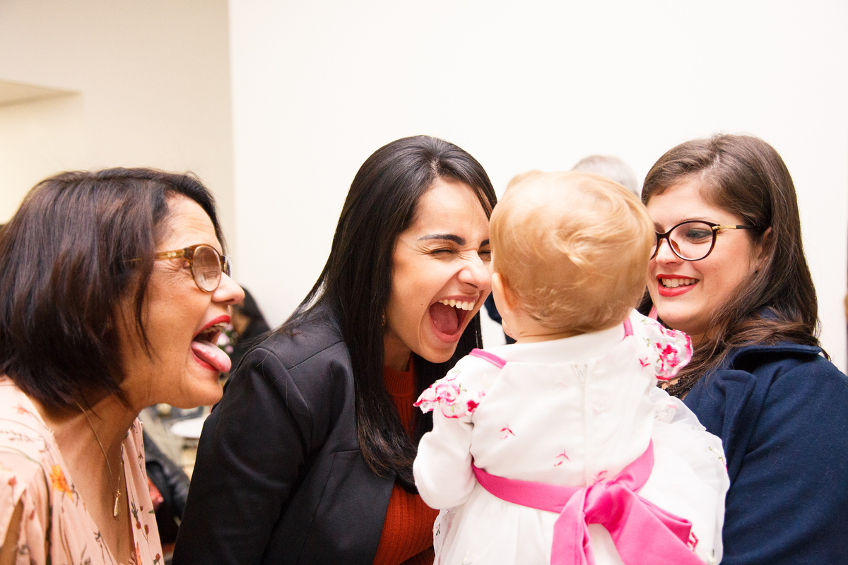 Adultos fazendo caretas para a bebê que se diverte no colo.
