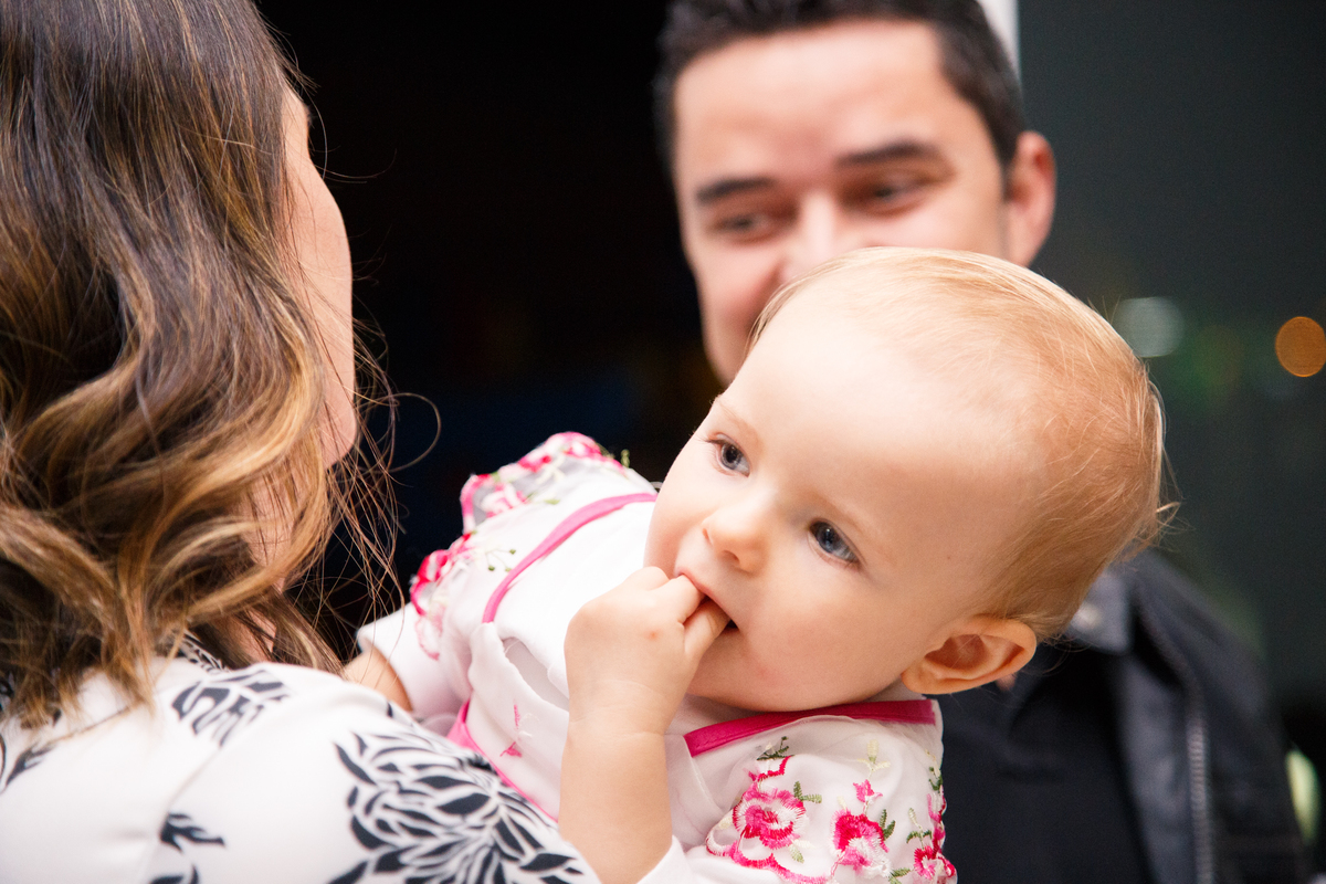 Bebê no colo de sua mãe olhando sobre o ombro dela algo que está acontecendo.