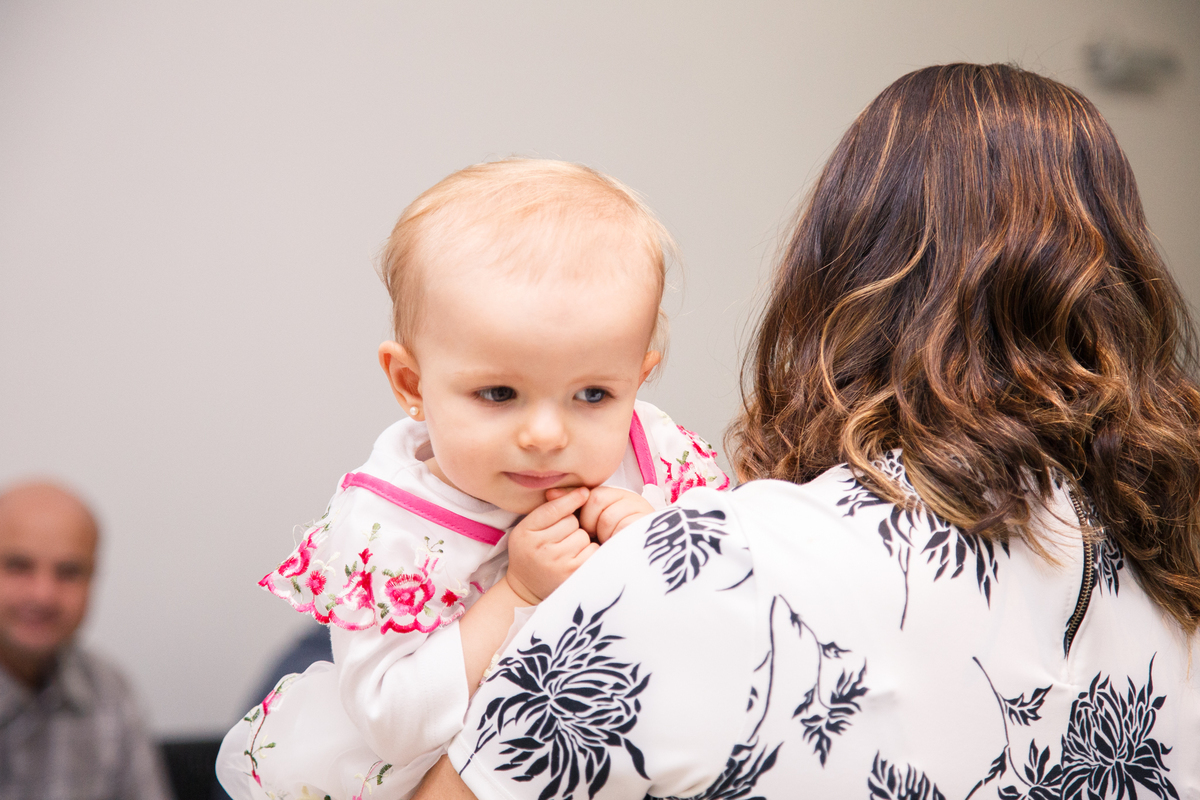 Criança no colo da mãe olhando por sobre o ombro dela com uma expressão pensativa e atenta.
