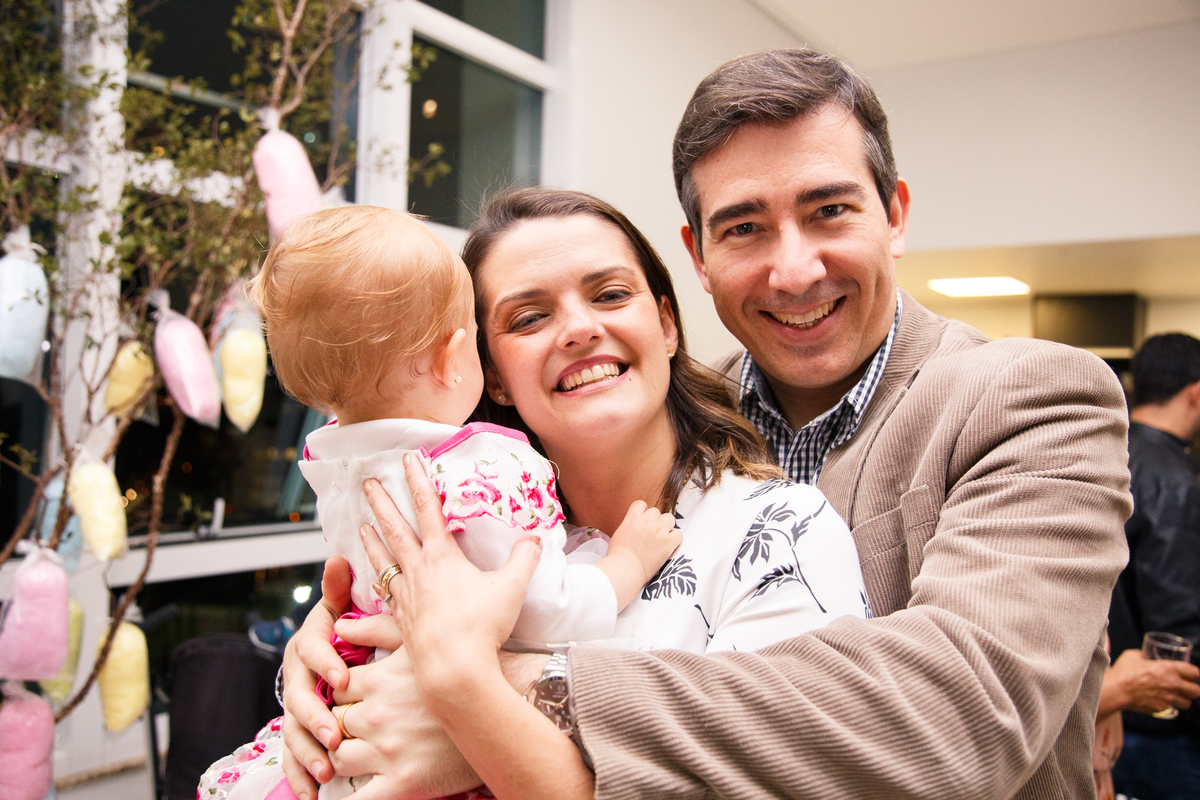 Mãe e pai abraçando a bebê e posando para foto durante aniversário de 1 ano.