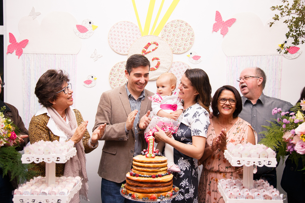 Família atrás da mesa do bolo cantando parabéns para a criança em seu aniversário de 1 ano.