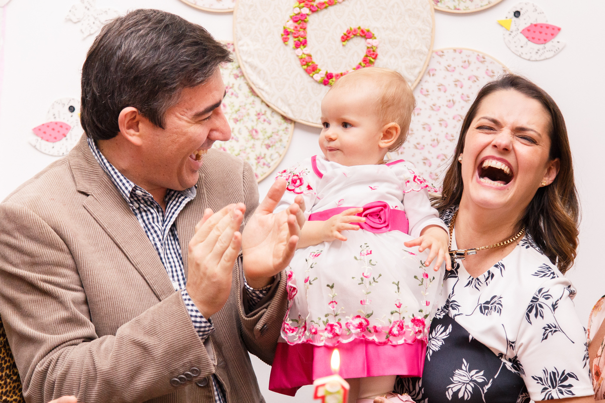 Pais rindo com sua filha no colo durante parabéns na festa de aniversário.