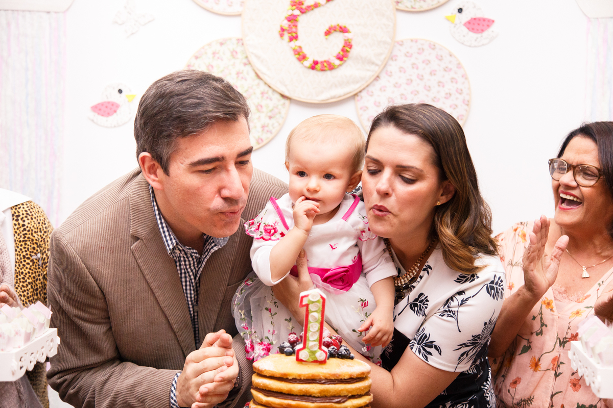 Pai e mãe soprando as velinhas para a filha que faz 1 ano.