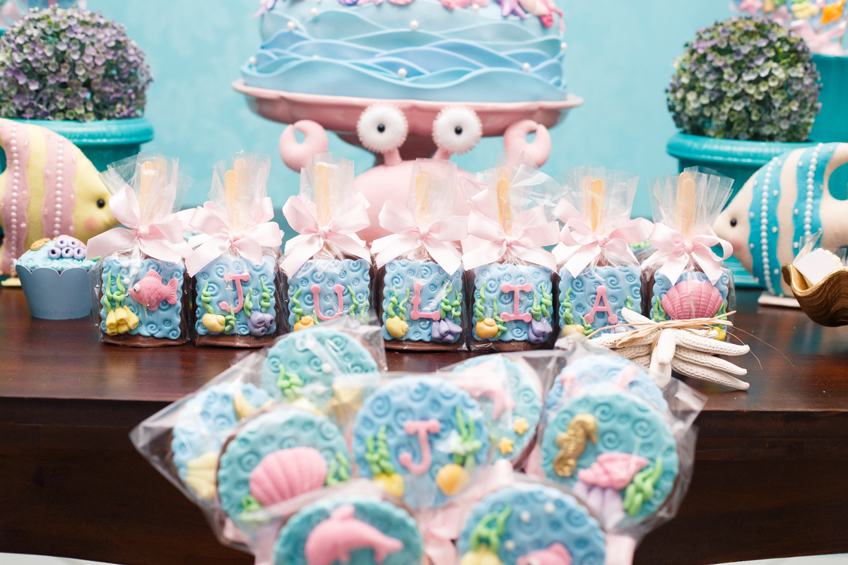 Detalhe da mesa do bolo em aniversário infantil com pirulitos de chocolate decorados no tema sereismo.