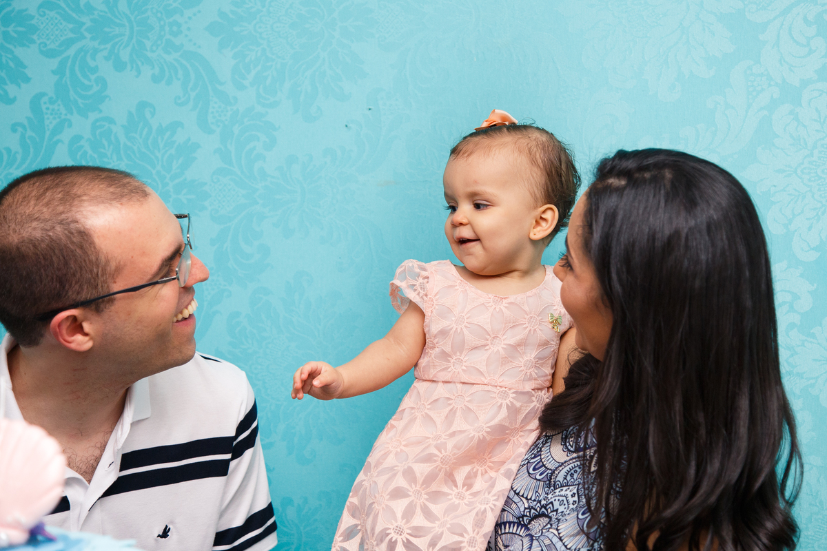 Bebê no colo da mãe sorrindo para o pai que faz gracinhas para ela.
