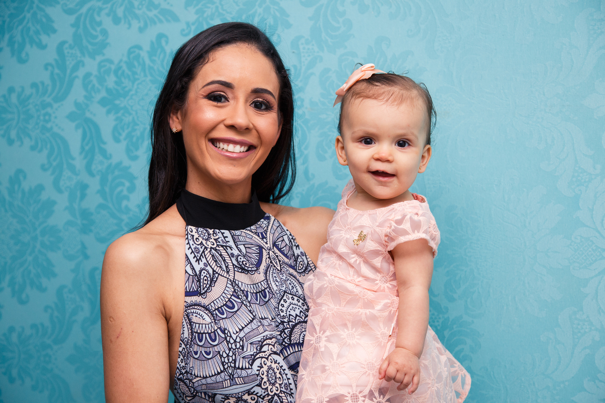 Mãe com sua bebê aniversariante no colo, ambas olhando para a câmera e sorrindo.
