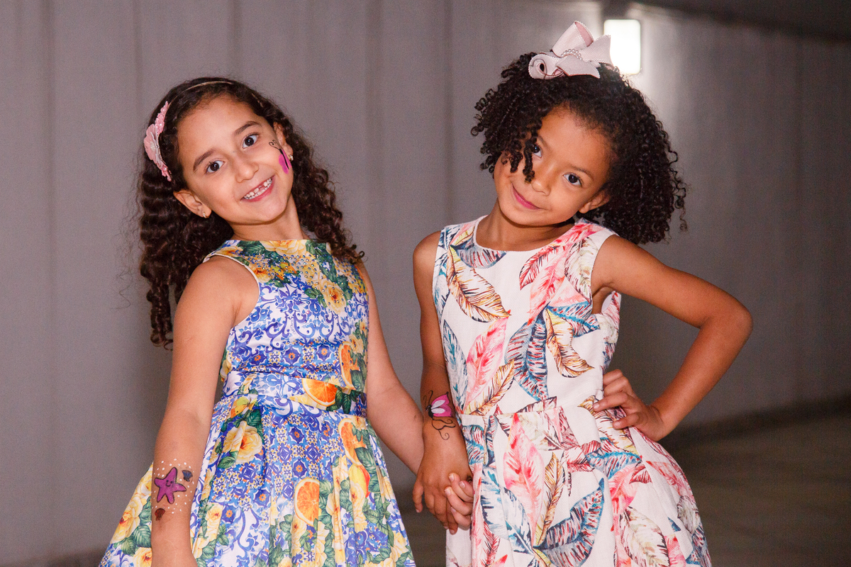 Duas priminhas em aniversário infantil posando para a foto com a mão na cintura.