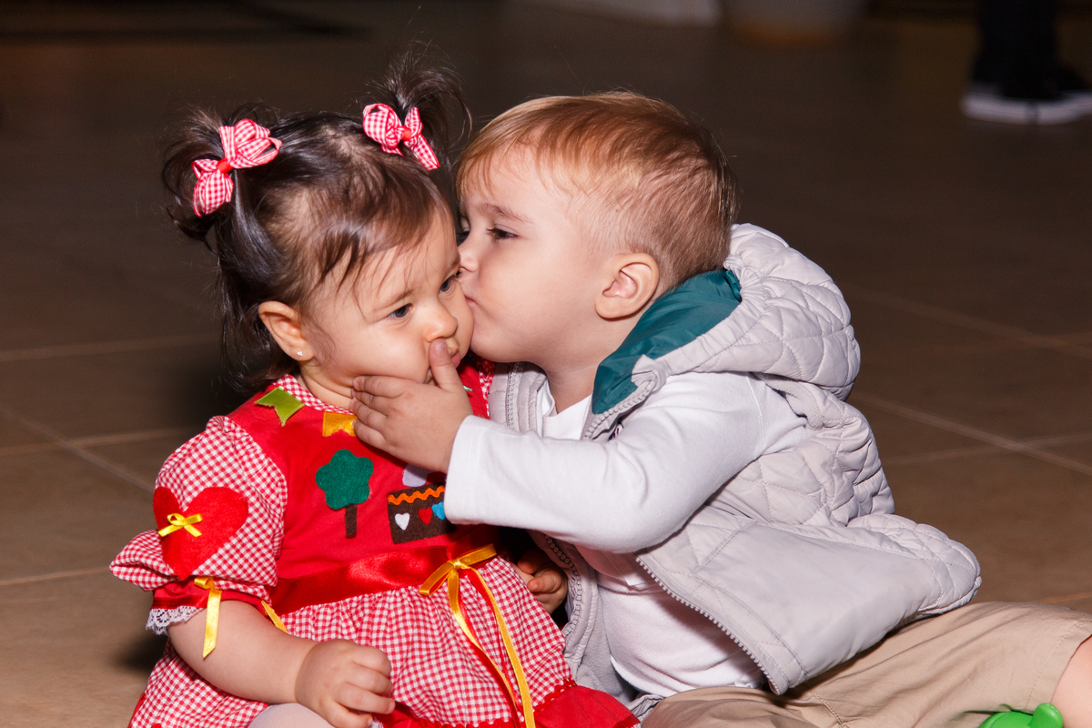 Priminho dando uma beijo na bebê aniversariante durante a festa de aniversário.