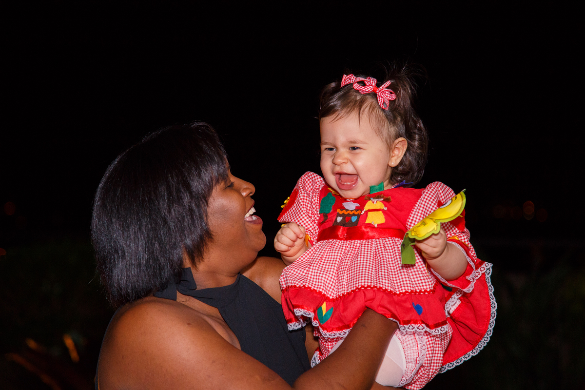 Bebê no colo de uma tia que brinca de aviãozinho e faz a bebê dar gargalhada.
