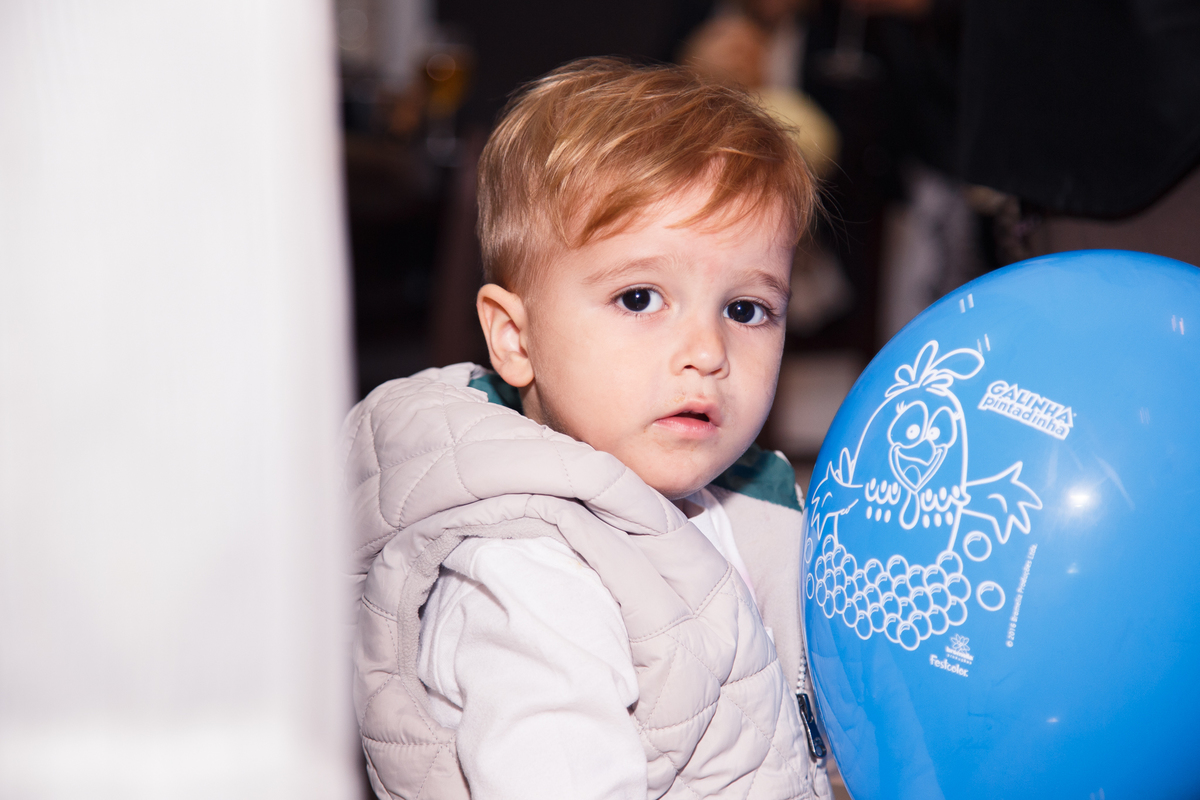 Criança segurando uma bola sentada, encostada em uma pilastra, olhando para a câmera.