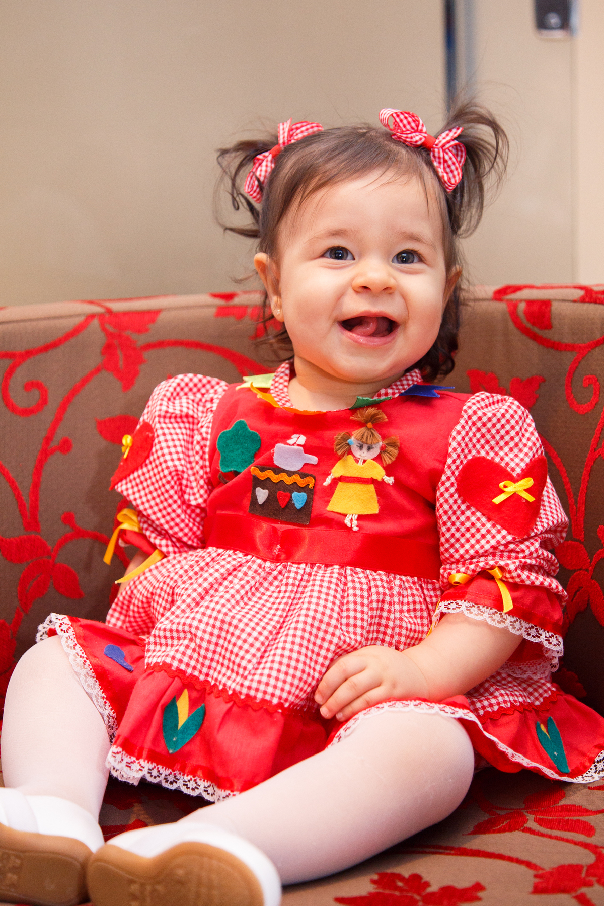 Bebê aniversariante sentada em uma poltrona sorrindo para a avó que não aparece na foto.