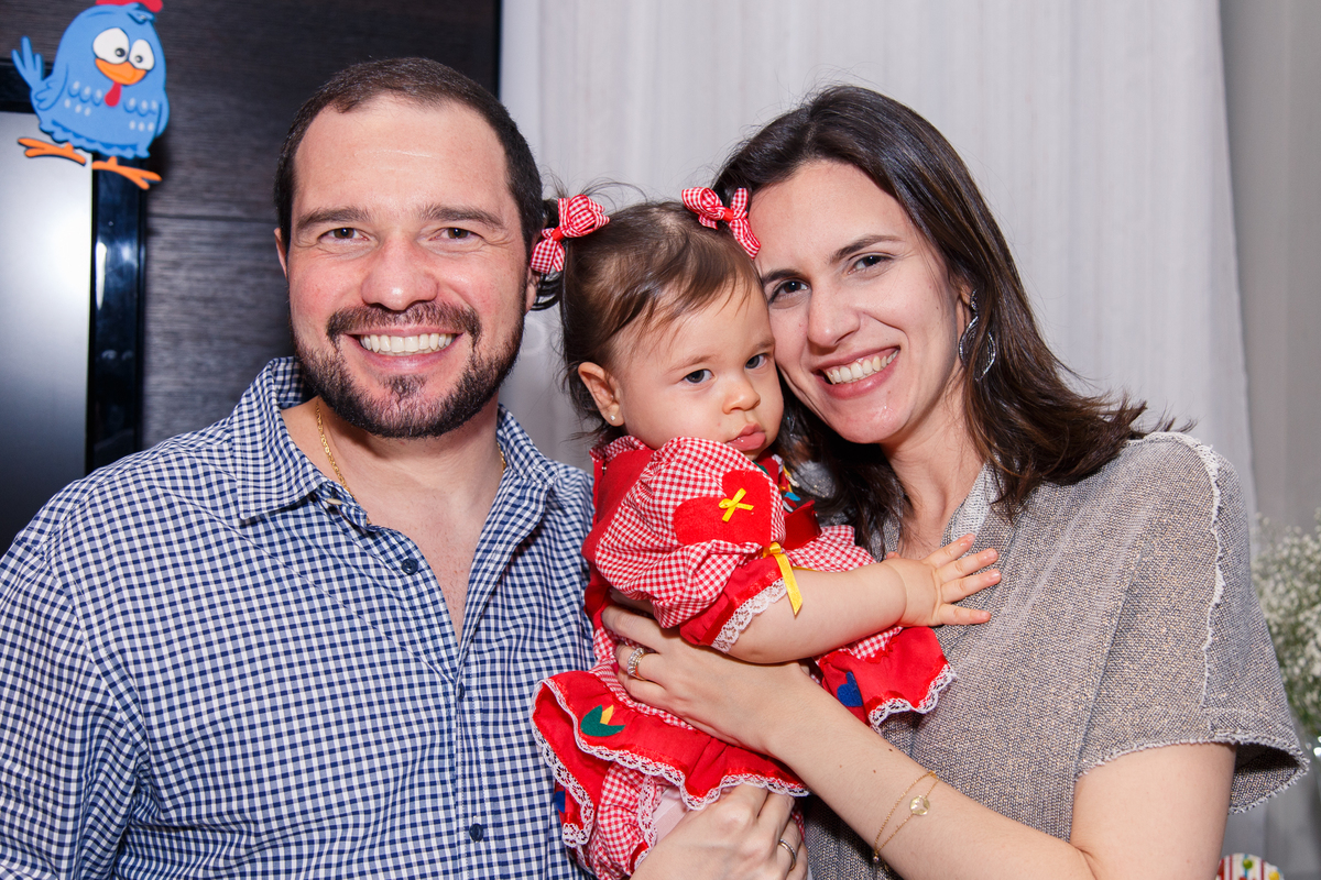 Pais com sua bebê aniversariante atrás da mesa do bolo logo antes de cantar parabéns.