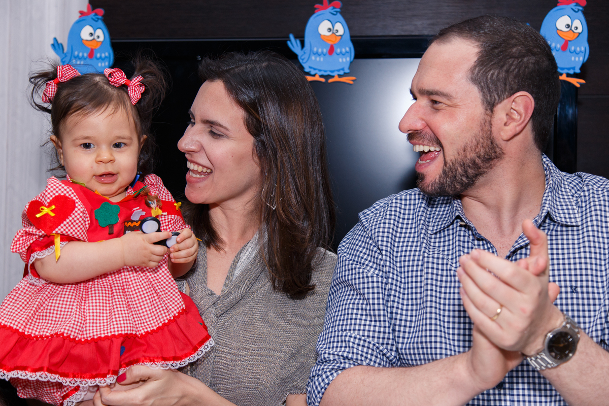 Pais com a bebê no colo cantando parabéns em sua festa de aniversário de 1 ano.