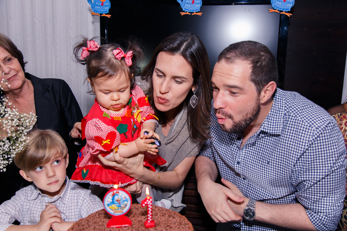 Pais com a bebê no colo assoprando a velinha de seu aniversário de 1 ano.