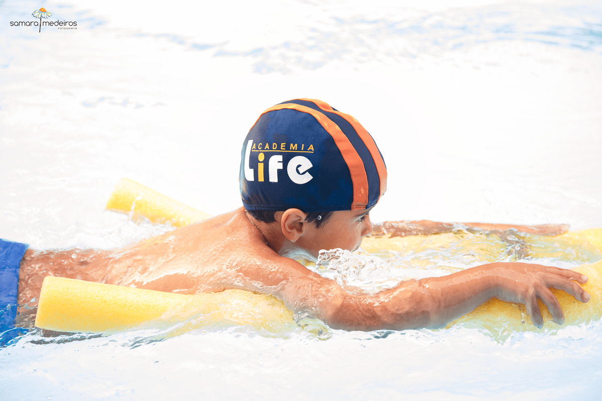 Criança nadando usando um espaguete amarelo.