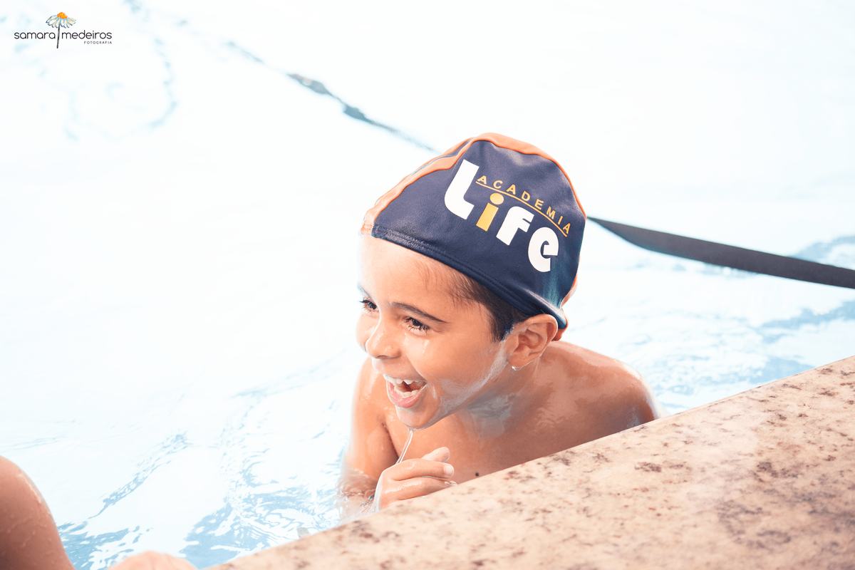 Criança dentro de uma piscina rindo e brincando com outra criança.