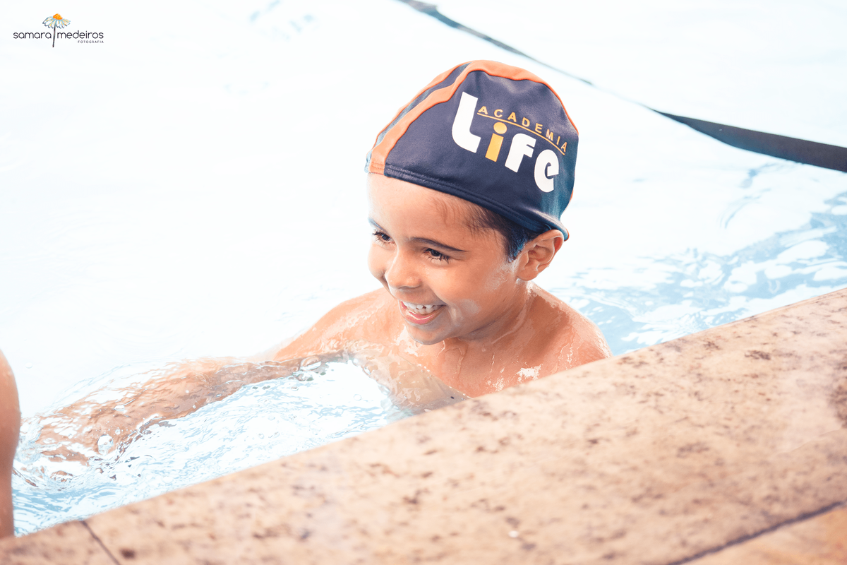 Criança dentro de uma piscina brincando com outra criança e rindo.