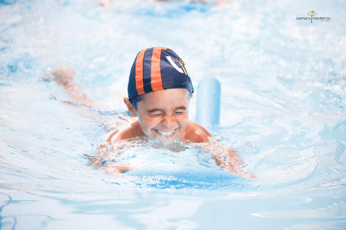 Criança nadando usando um espaguete, com a água batendo em seu rosto.