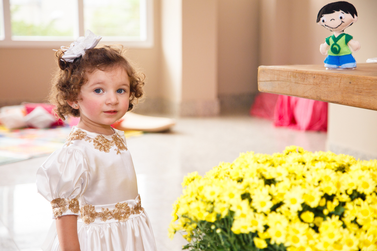 Criança aniversariante de 2 anos de pé ao lado da mesa do bolo em sua festa.