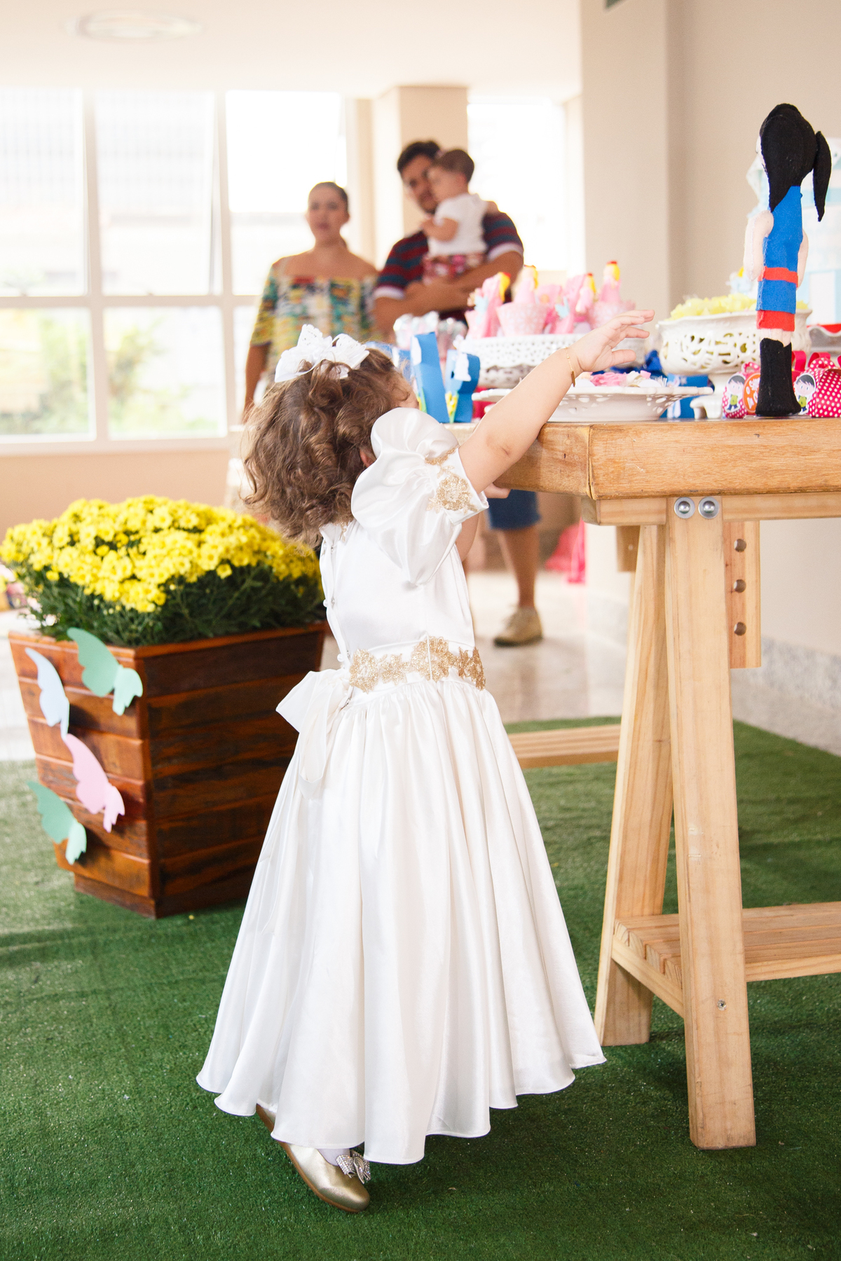 Criança na ponta dos pés tentando alcançar um doce na mesa do bolo de sua festa de 2 anos.