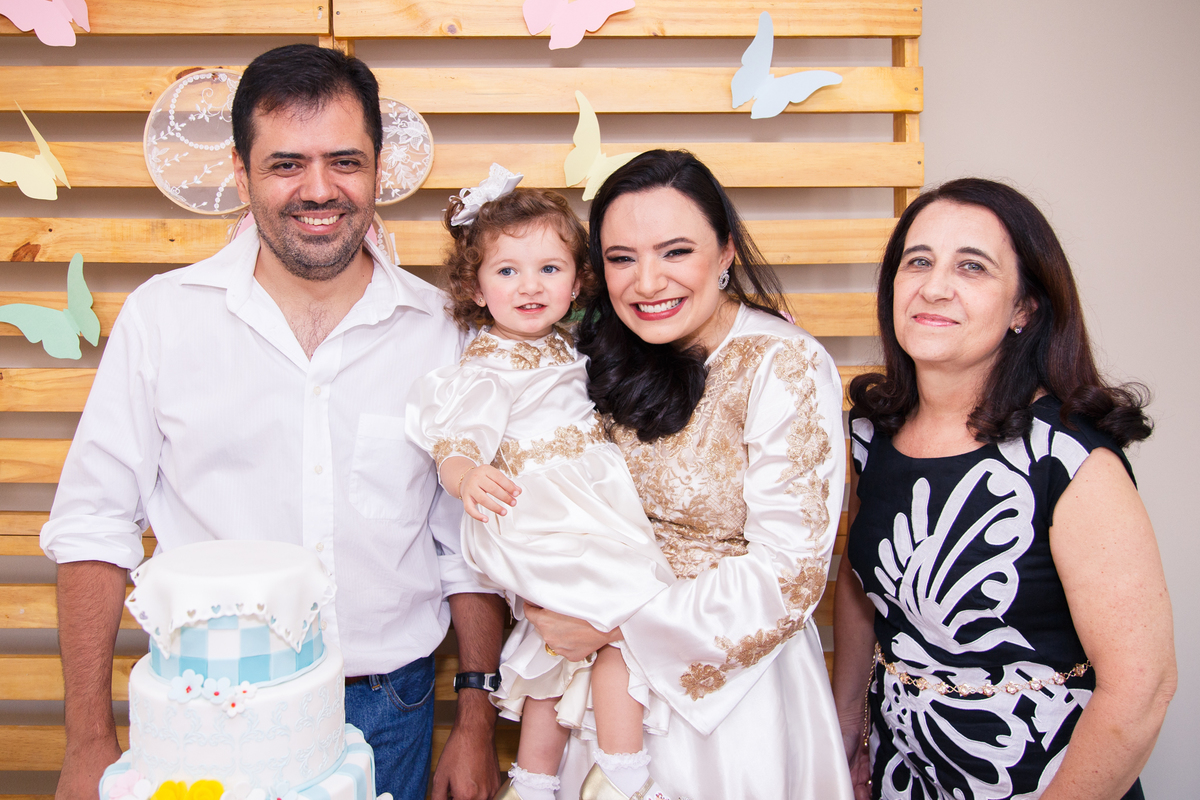Criança no colo de sua mãe com o pai e avó em frente ao painel da mesa do bolo.
