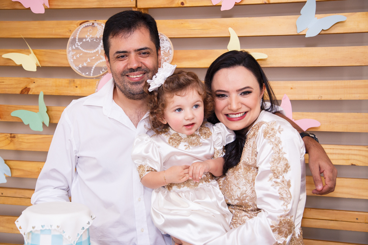 Família em frente ao painel da mesa do bolo do aniversário de 2 anos da criança que está no colo.