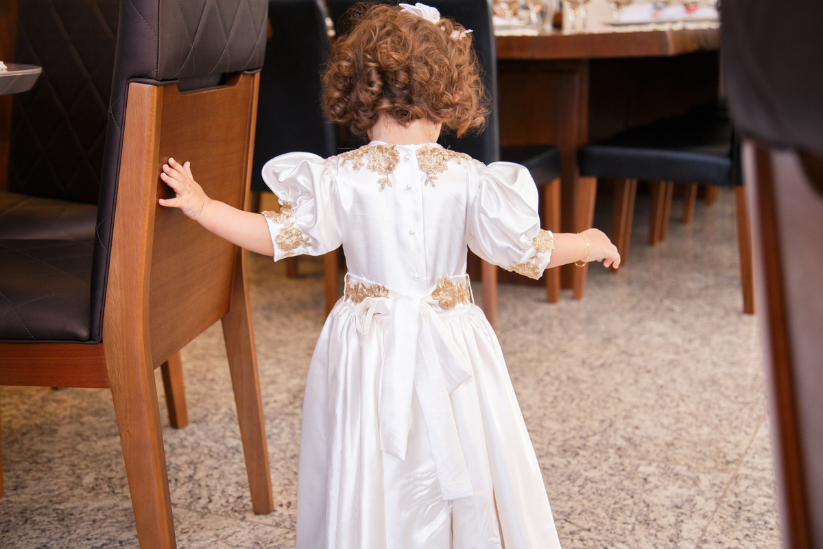 Criança de pé, de costas caminhando entre as cadeiras de sua festa de aniversário de 2 anos.