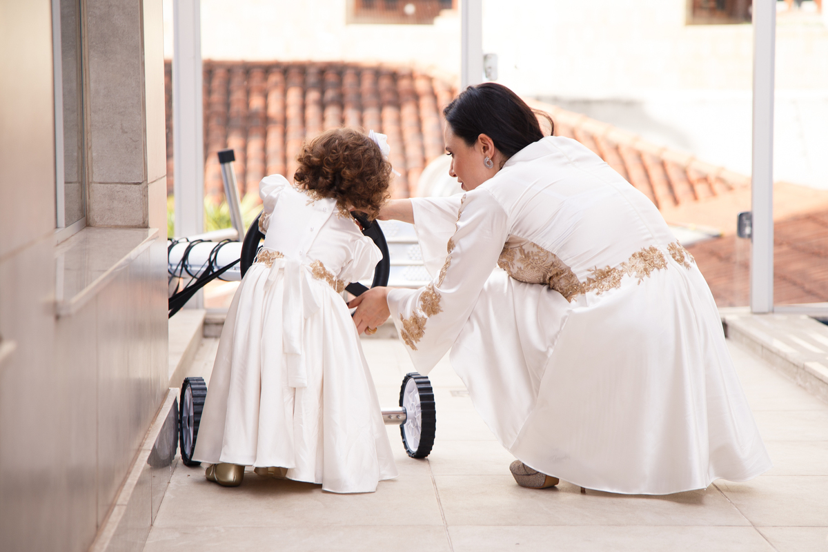Criança e sua mãe de costas, a criança de pé e a mãe abaixada brincando com um 