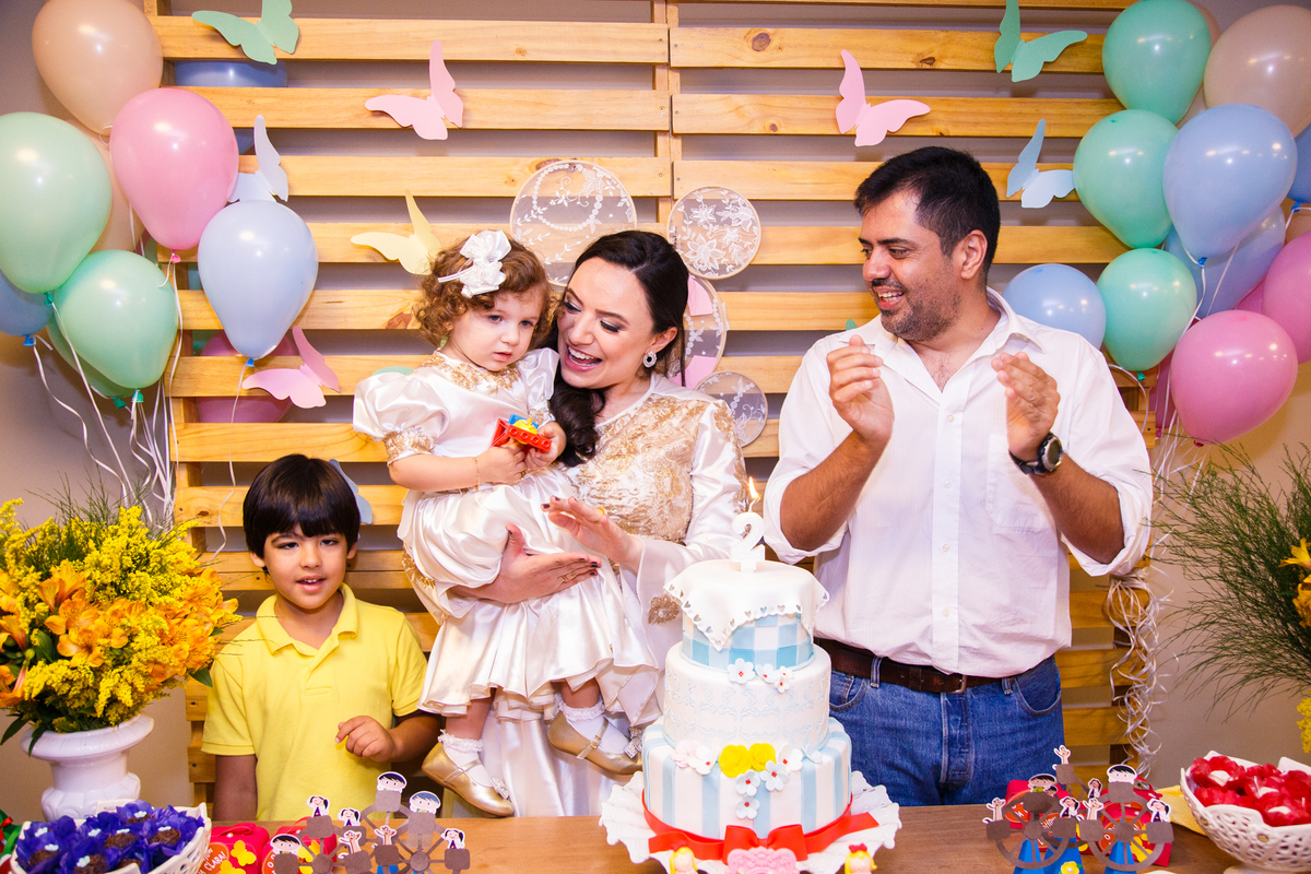 Criança e seus familiares cantando parabéns atrás da mesa do bolo em sua festa de 2 anos.