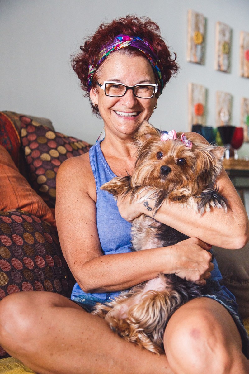 Tutora sentada no sofá segurando sua cachorrinha Yorkshire, enquanto olha para a foto e sorri.