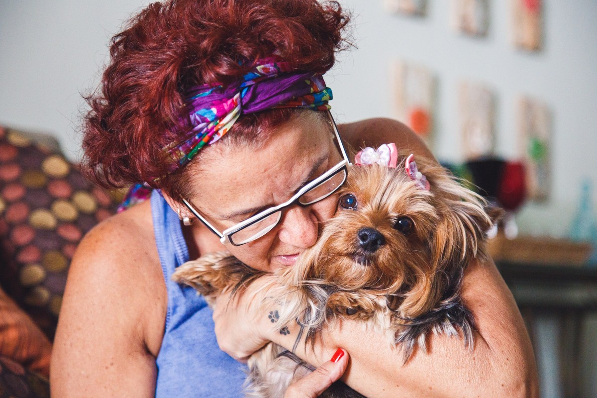 Tutora sentada no sofá com sua York no colo dando um beijo nela.