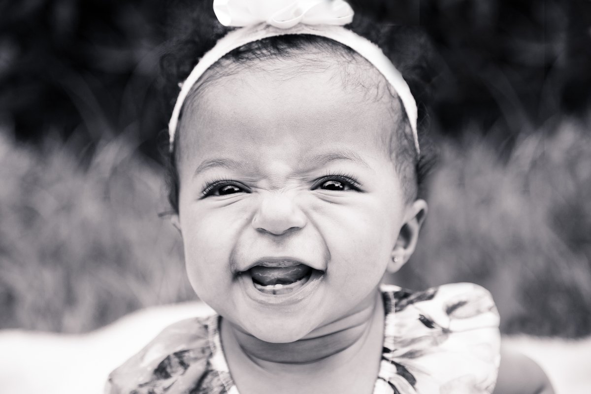 Foto em preto e branca de uma bebê sorrindo, enrugando o nariz, em ensaio de família em BH.