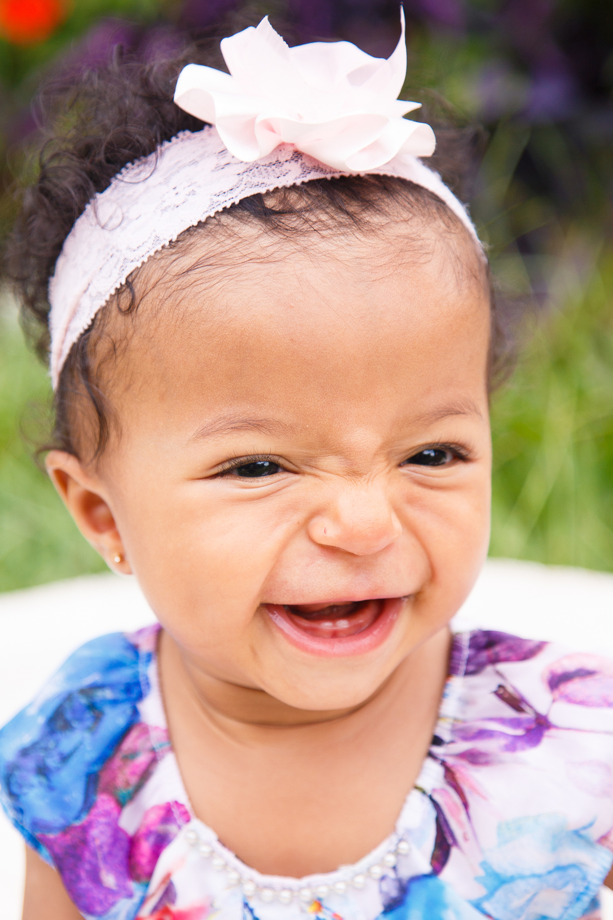 Bebê sorrindo da irmã, que não aparece na foto, fazendo gracinhas para ela, durante ensaio fotográfico de família.