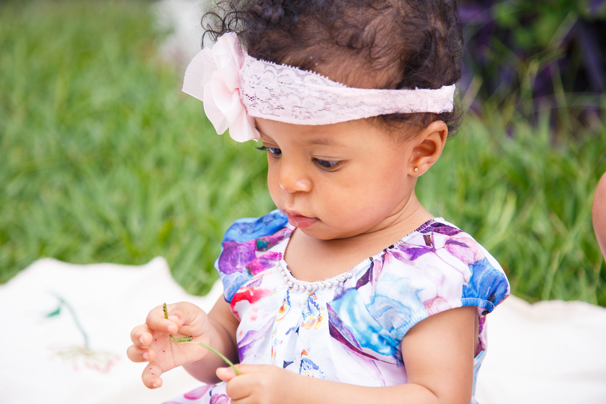 Bebê sentada na grama e brincando concentrada com um pedaço de capim.