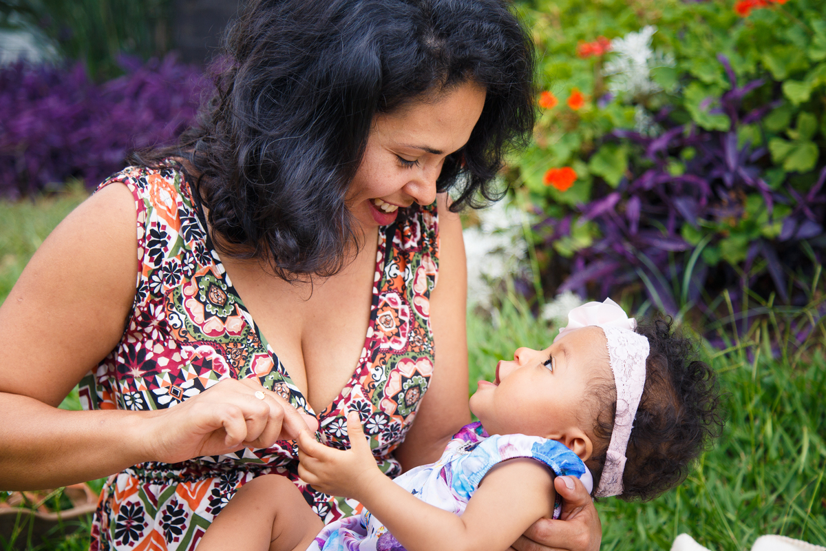 Mãe sentada na grama brincando com sua bebê no colo, ambas sorrindo.