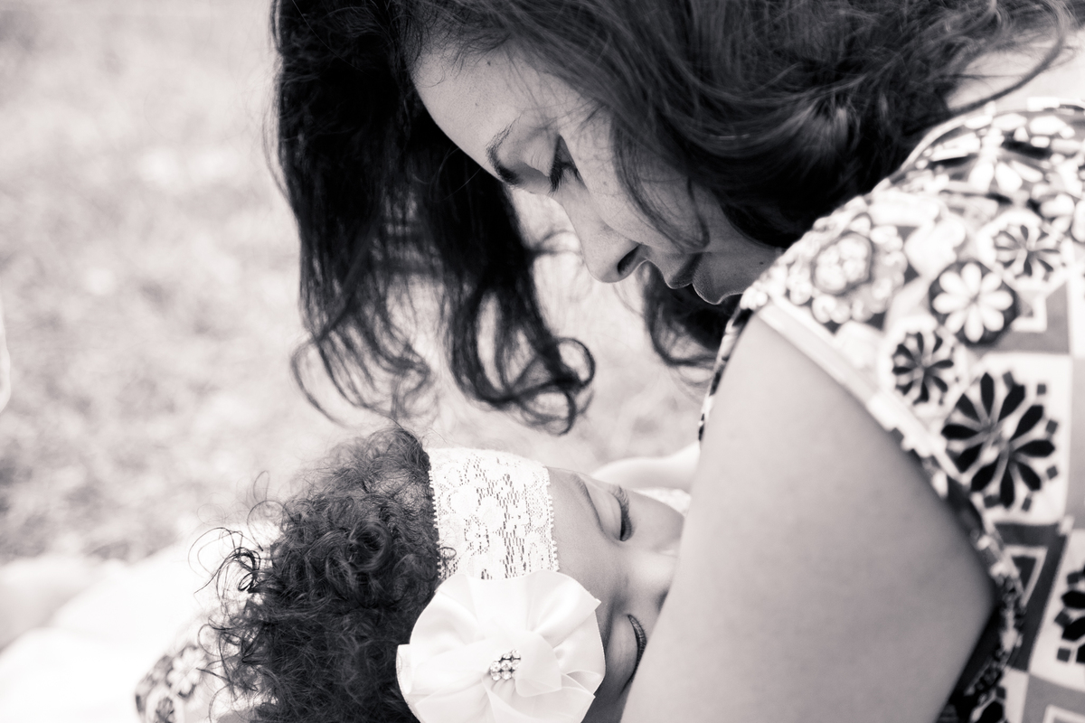 Foto em preto e branco de uma bebê mamando e sua mãe olhando para ela.
