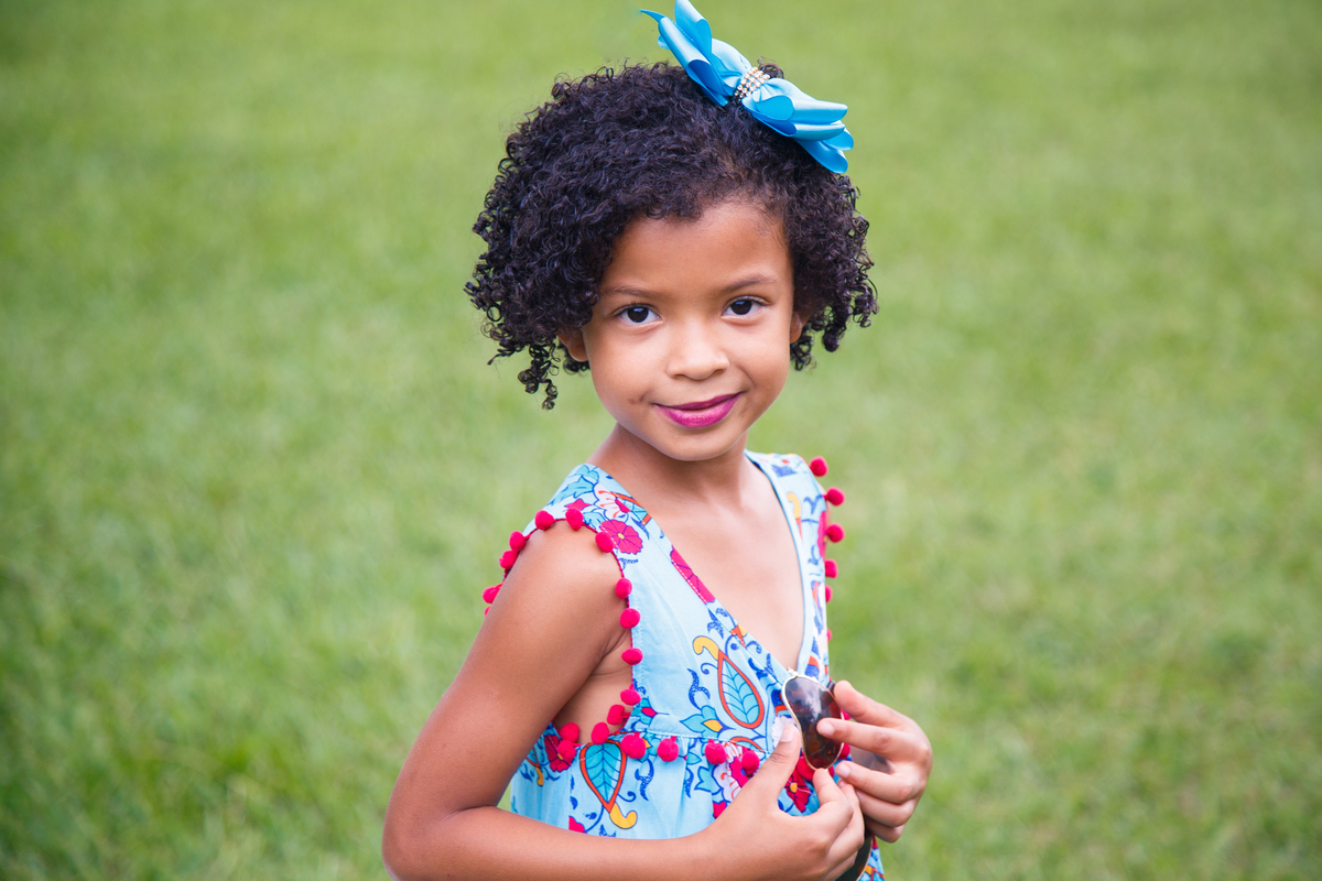 Criança de pé na grama posando para foto em ensaio fotográfico de família.