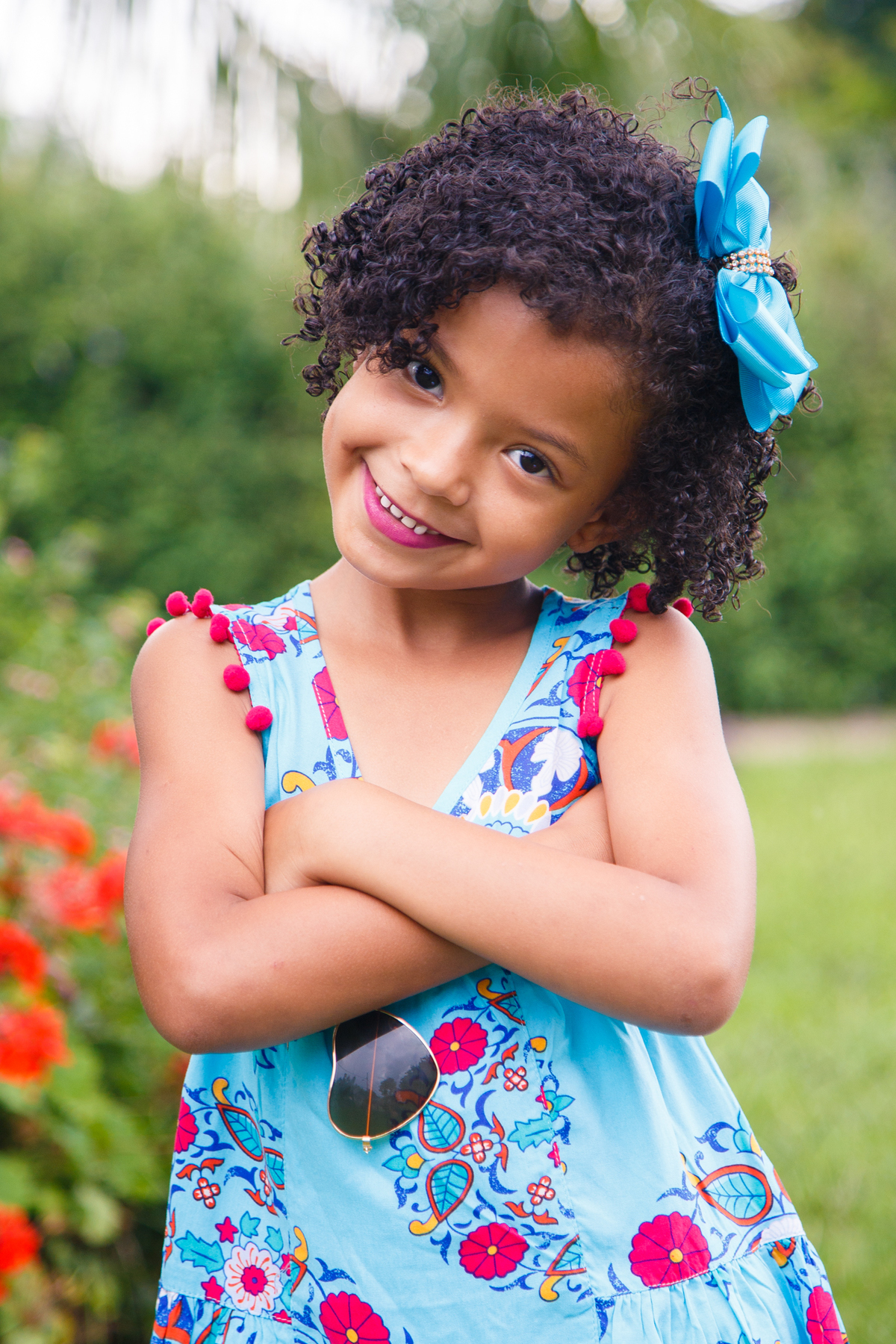 Criança fazendo pose para foto, olhando para a câmera com os braços cruzados e a cabeça de lado, sorrindo.
