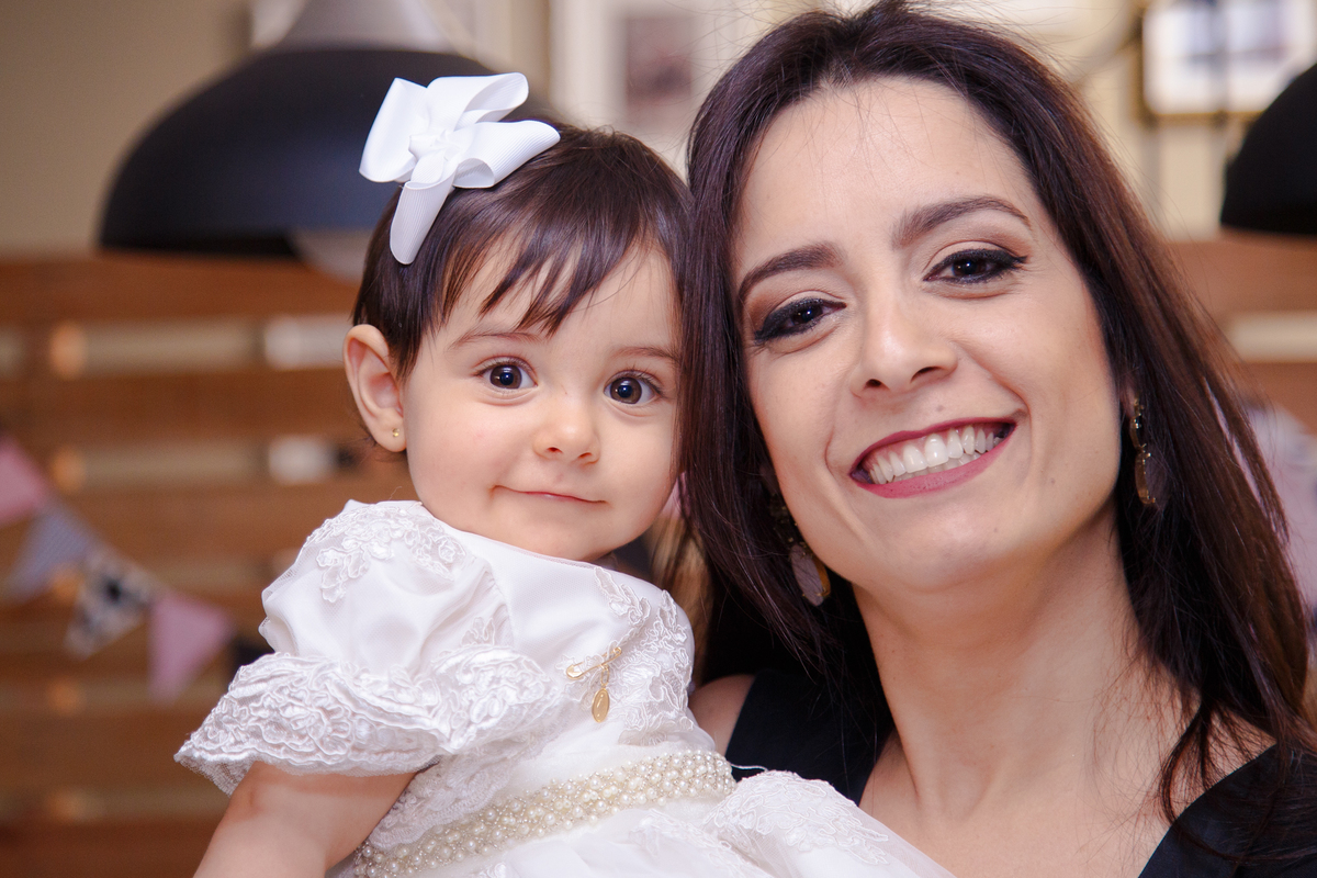 Bebê aniversariante no colo de sua mãe, ambas olham para a foto e sorriem.