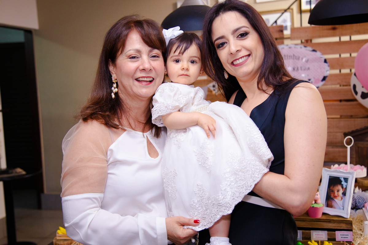 Três gerações, mãe, filha e neta bebê que está completando 1 ano, todas olhando para a câmera.