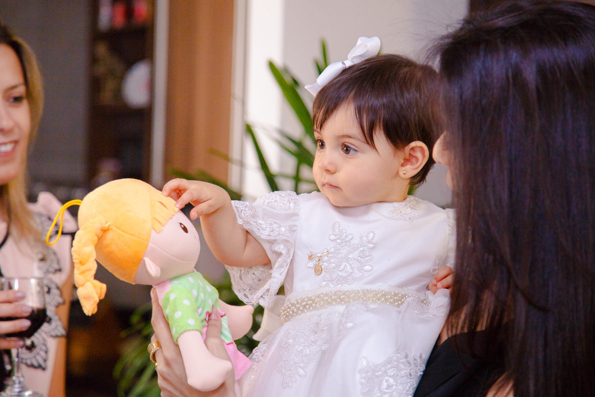Bebê aniversariante recebendo de presente uma boneca e passando a mão nela.
