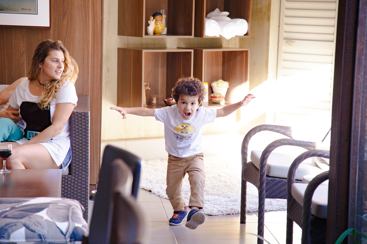 Criança brincando de imitar um dinossauro, com os braços abertos, as mãos imitando garras e a boca aberta em um rugido.