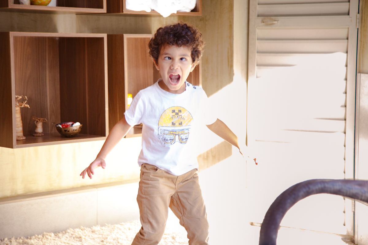 Criança imitando um dinossauro com a boca aberta em um rugido e os olhos fingindo de vesgo.