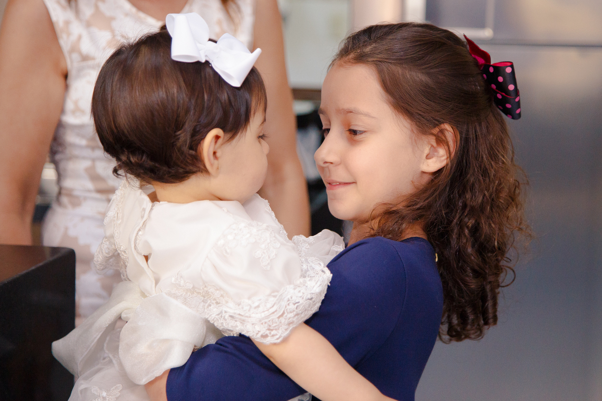 Bebê no colo de sua priminha, as duas se observando.