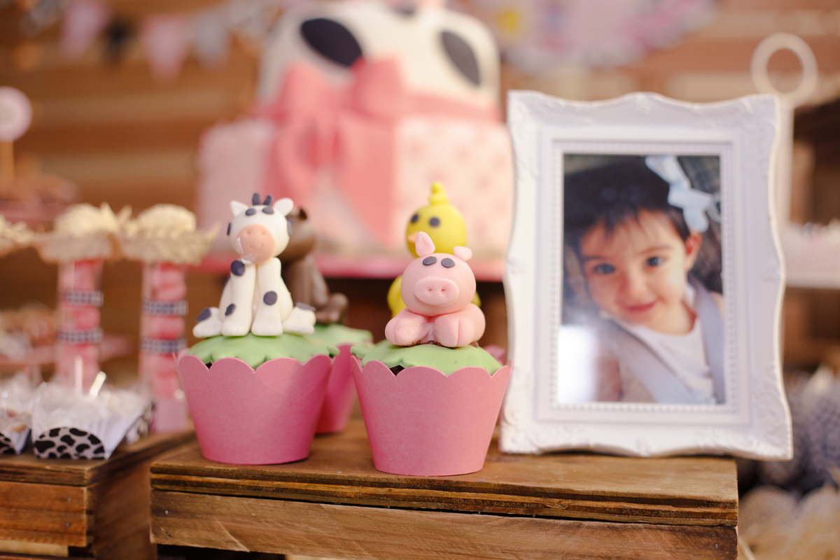 Doces personalizados com animais de fazendo em cima, vaca, porco e pintinho. Uma foto da aniversariante está em um porta retratos ao lado.
