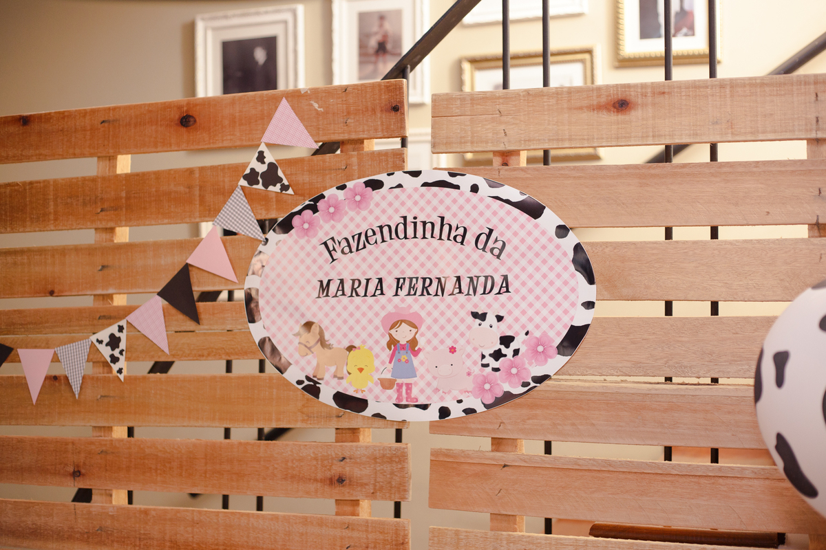 Painel atrás da mesa do bolo com o escrito Fazendinha da Maria Fernanda, em um aniversário infantil.