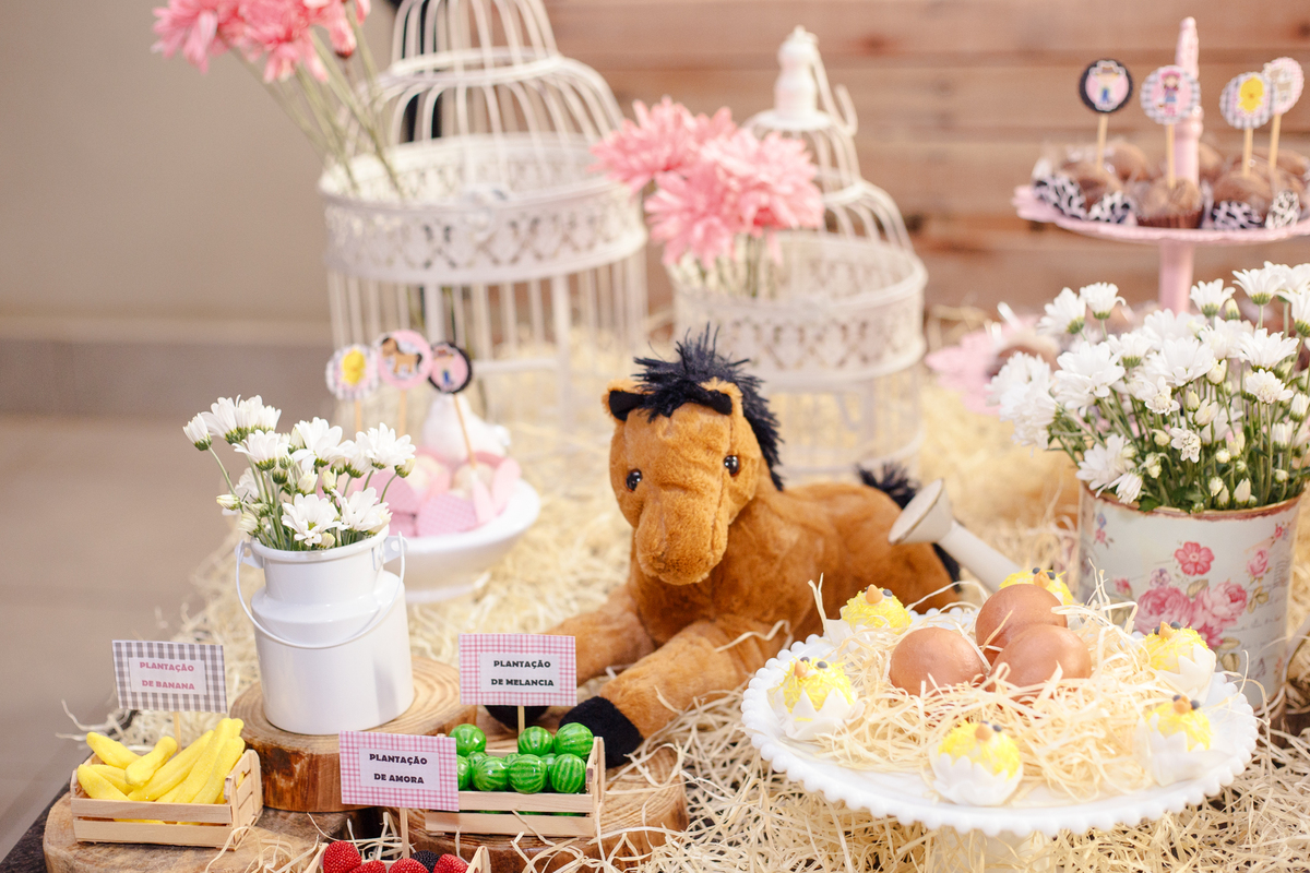 Detalhe da decoração no tema fazendinha, com um cavalo de pelúcia, ovos e pintinhos e algumas mini caixas de madeira com frutas.